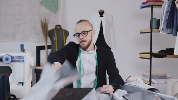 Atelier. Cansado designer de moda e alfaiate na mesa de trabalho com tecidos no estúdio. Conclusão do dia útil — Vídeo de Stock