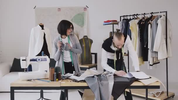 设计师.舞蹈和有趣的工作两个设计师的衣服在一个创造性的工作室裁缝。时尚服装设计师男人和女人正在工作室的布测量。好工作 — 图库视频影像