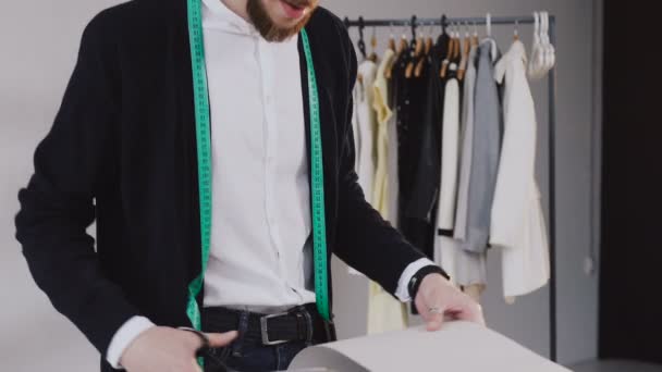 Fiatal férfi tervező szalag-line a a nyak állandó ruhakészítés stúdió és vágott ollóval egy minta egy kapszulakollekciót. Férfi szakállas divat tervező és személyre szabott, az atelier kivágása a — Stock videók