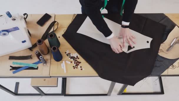 Ansicht des Modedesigners oder Schneiders, der ein Muster auf ein braunes Stück Gewebe schneidert. Schneiderin benutzt Kreide und hält Skizze auf Textil — Stockvideo