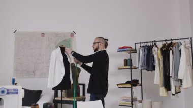 Profesyonel beyaz terzi ya da moda tasarımcısı manken satırda yeni bir moda koleksiyonu işçiliği süre ölçme ile tedbirleri almak. Şık, konforlu stüdyo. İşçilik, Atelier içinde çalışma