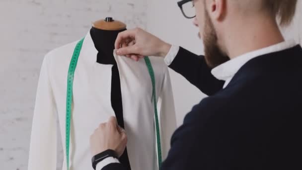 Portrait of a tailor while making a white jacket using the tape measure. Close-up of a professional caucasian tailor taking measures with measuring line on mannequin while crafting a new fashion — Stock Video