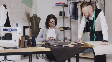 Takım çalışması iki terzi ve terzi kim gülümseme ve yeni bir koleksiyon dikiş üzerinde çalışıyor. Terzi makas ile desen keser ve stilist iş akışını izler