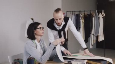İki beyaz moda tasarımcıları farklı terzilik araçları ve elbise ile güzel ofiste oturan kumaş deseni ile çalışma terzi. Terzi ve terzi stüdyoda işyerinde