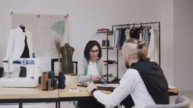 Moda tasarımcıları farklı terzilik araçları ve giysileri ile ofiste kumaş seçimi iki kişi. Genç kadın ve erkek moda tasarımcıları veya terziler güzel oturan kumaşlar ile çalışma