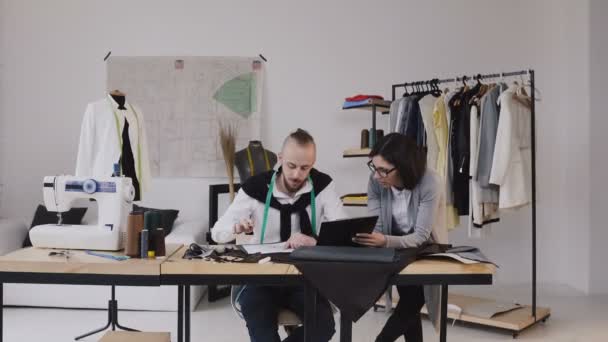 Modedesigner, die im Büro mit verschiedenen Schneiderwerkzeugen und Kleidungsstücken arbeiten. zwei Modeschöpfer Mann und Frau diskutieren Design neue Kollektion — Stockvideo