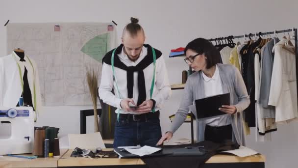 Meisjes assistent, toont ontwerper schetsen op vellen papier. Mode-ontwerper in zijn studio foto's miniaturen op de telefoon. — Stockvideo