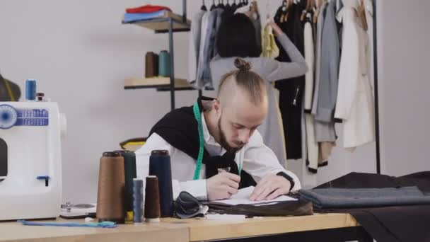 Két divattervezők dolgozik az új kollekció. Pár divattervezők dolgozik a műhelyben. Stílusos szakállas ember van folyamatban új ruhák-gyűjtemény létrehozása — Stock videók