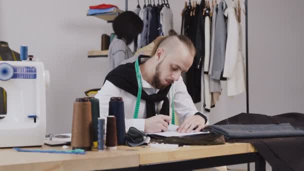 Joven hermosa mujer está de pie en un pequeño estudio elegante y elegir el vestido con el diseñador. La mujer elige el vestido. Bastante hembra está buscando equipo tratando de entender si este color se adapte a su — Vídeos de Stock