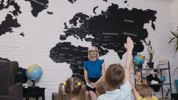 Lärare grundskola i glasögon under lektionen kontrollerar kunskap av hans elever som höjer händerna upp. Barn öka händer att veta svaret på frågan vem frågar läraren — Stockvideo