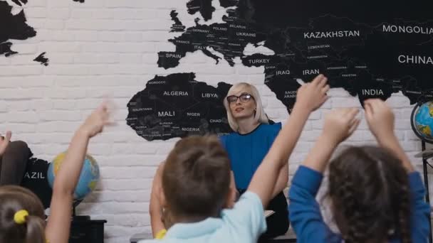 Una linda profesora de gafas durante la lección y comprueba el conocimiento de sus alumnos que levantan las manos. Niños levantando las manos sabiendo la respuesta a la pregunta quién le hace al maestro — Vídeos de Stock