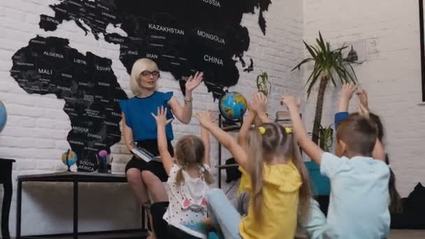 Une enseignante mignonne s'amuse à sourire aux enfants pendant la leçon et vérifie les connaissances de ses élèves qui lèvent la main. Les enfants levant la main connaissant la réponse à la question qui a posé la — Video