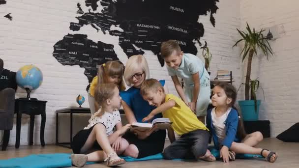 Group of beautiful kids talking about book with nursery teacher in preschool. Happy child day care worker with children reading a book in elementary school or primary school in geography class — Stock Video