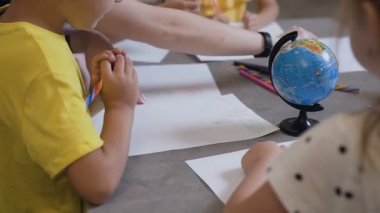 Bir grup çocuk ve bir öğretmen beyaz renkli kalemler kullanarak kağıt üzerinde çizin. İlkokul çocukları sınıfta yardımcı öğretmen ile çizim