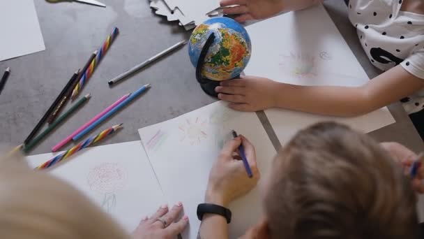 Vista superior. En la lección de dibujo, los niños se sientan a la mesa y dibujan con el maestro. Los niños pintan con lápices. Alumnos con profesor dibujan sobre papel blanco con lápices de colores — Vídeo de stock