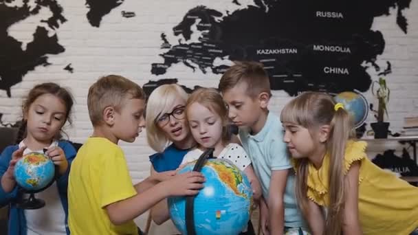 Close-up. An attractive teacher are educating five of his pupils at elementary school and using a globe to teach them about the world. Geography lesson. Boys, girls and their young teacher study the — Stock Video