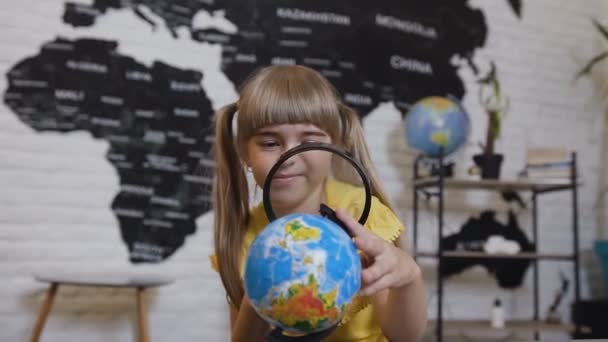 Portrét roztomilá dívka, která hraje při pohledu zvětšovací skla. Dívka Odhlédneme zvětšovací sklo a studuje globe nebo mapa světa — Stock video