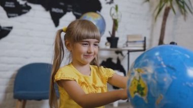 Sarı tişört içinde tatlı bir kız Coğrafya sınıfta masada oturur ve küre veya dünya harita merakla okuyor. 6 yaş kız küre veya dünya harita katlanmış ve dünya çalışmaları