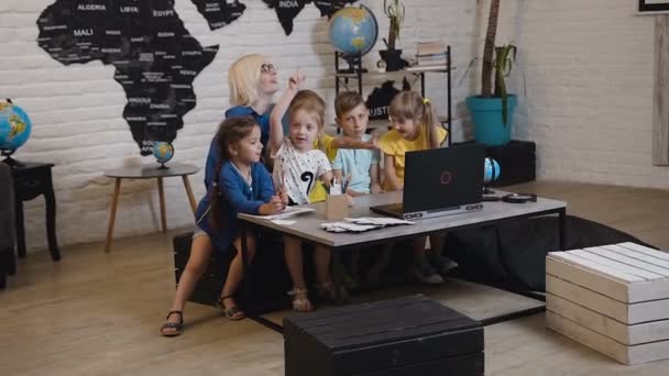 Professora com seus pequenos alunos diversão assistindo laptop na aula de geografia na escola primária. Professor e crianças usando laptop em sala de aula — Vídeo de Stock