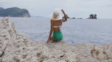 Arka görüş. Güneşten kadın giyinmiş bir mayo ve geniş bir hat, güzel genç bir rock ve seyir içinde hayat oturur sahiptir denizde. Adriyatik Denizi