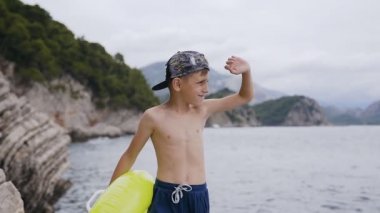 Sevimli küçük çocuk kayanın üzerinde durmak ve gün batımında denize bakın. Arayan denizde dalgalar şişme halka şirin bir çocukla portresi. 7-8 yaş çocuk yaz tatili