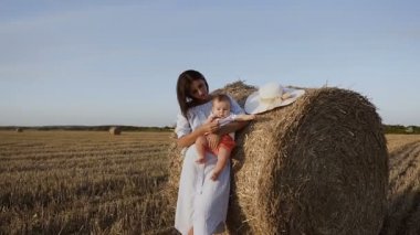 Gün batımında alanındaki oğlu olan kadın. Şirin esmer elbiseli bir balya saman yakın alanda, oğulları üzerinde elele ve onunla payet ile oynamak