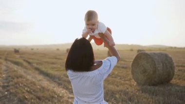 Bir ışık içinde güzel kadın onun büyüleyici erkek bebek ve çevresinde başlar ve gülümsüyor yüksek yükseltir. Gün batımında oğlu alanında oynamaktan mutlu genç kadın vakit