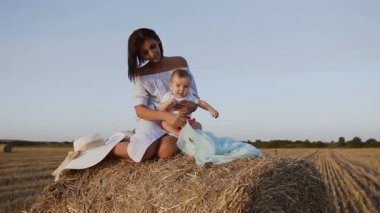 Küçük oğlu güzel bir kızla bir alanı bir haystack ve onunla oynarken oturuyor. Bebeğini doğa alanında Toskana İtalya ile mavi elbiseli çekici genç kadın