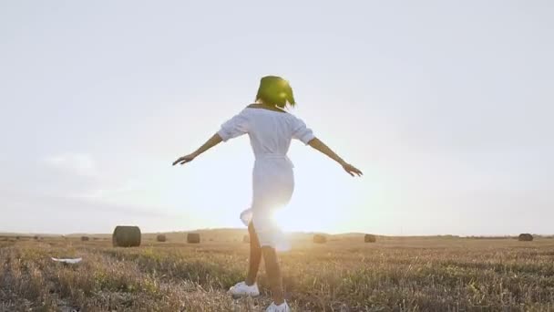 En ung söt kvinna glatt kör igenom ett gyllene fält med halmbalar vid solnedgången. Glad tjej njuter och springa runt själv på naturen. Vacker ung kvinna som har kul i ängen — Stockvideo