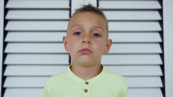 Retrato de un niño lindo que mira y sonríe en la cámara en el fondo blanco. Niño de 5 a 6 años. Los jóvenes y las emociones, el retrato del niño hermoso 5-6 años mirando a la cámara — Vídeos de Stock