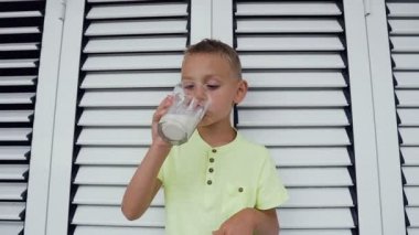 Genç beyaz çocuk beyaz süt içiyor. Sevimli çocuk t-shirt beyaz zemin üzerine bir bardak taze süt içiyor