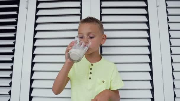 Der junge kaukasische Junge trinkt ein Glas weiße Milch. Netter Junge im T-Shirt trinkt ein Glas frische Milch auf weißem Hintergrund — Stockvideo