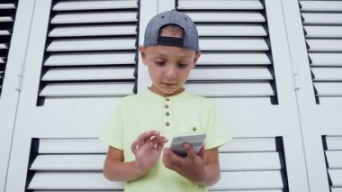 Beyaz arka plan üzerinde izole Smartphone oyun oynamayı memnun şirin küçük bir çocuk portresi. Smartphone üzerinde son derece online oyunlar oynayan çocuk konsantre