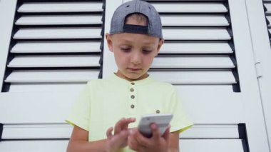 Genç Genç şapkalı beyaz kapı arka plan üzerinde izole Smartphone cep telefonu ile oyun oynama. Smartphone teknoloji ile oynayan çocuk. Yakın çekim Genç çocuğun onun smartphone üzerinde mesaj yazmak