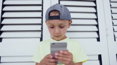 Kap ve t-shirt çocukta bir smartphone önünde tutuyor ve iskambil video oyunu, beyaz bir arka plan üzerinde yoğunlaşmıştır. Sevimli çocuk t-shirt ve iskambil online spor izole Smartphone'da kap