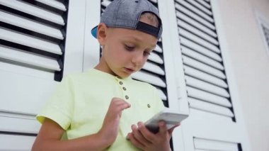Yüzü ve elleri bir 5-6 yaş çocuk evinde açık duran ile bilgisayar oyunu oynamak kapatın. Telefon kullanarak çocuk. Duran yakın pencere beyaz smartphone ile bir çocuk portresi. Kavramı