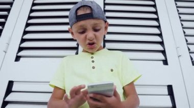 Küçük çocuk oyun oynarken cep telefonuyla Close-up. Akıllı telefon ekranında, güneşli yaz tatillerini zevk görünümlü, güzel çocuk T-shirt giyen kullanmanın portre olduğunu