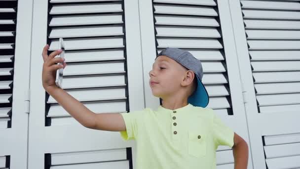 Joyeux petit garçon faisant selfie photo avec smartphone à la maison isolé sur fond blanc. Adolescent heureux faisant selfie photo pour les réseaux sociaux — Video