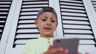 Komik şirin küçük çocuk smartphone vasıl oyun oynuyor. 5-6 yaşından küçük çocuk çok yakın telefon yüzüne tutar. Telefonda online oyun sırasında çocuğun duygular