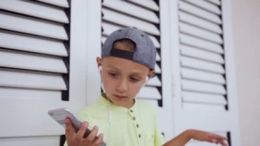Gri smartphone ve beyaz arka planda kapalı dans kulaklıklar müzik dinleyen güzel küçük çocuk t-shirt ve şapka. Çekici bebek çocuk dans müzik dinlerken