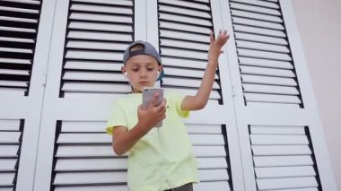 Bir hippi çocuk t-shirt ve şapka portresi beyaz arka plan üzerinde başını sallayarak dans kulaklık ile Smartphone cep telefonu ile en sevdiğiniz müzik dinliyor. Duygular kavramı