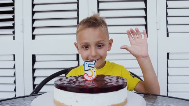 Lindo niño feliz celebrando su quinto cumpleaños, delante de él delicioso pastel con vela en forma de "5". Felices emociones de niño feliz en un cumpleaños, 5 años, pastel — Vídeo de stock