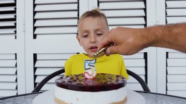 Masada oturan ve üfleme küçük çocuk Doğum günü pastası mumlar. Mutlu yakışıklı 5 şeklinde mum ile lezzetli pasta önünde, Beşinci yaş gününü kutluyor