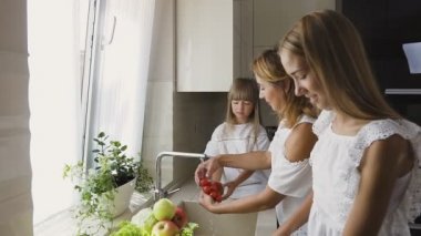 Çekici mutlu anne ve genç kızı sebze birlikte karıştırma salata, bir elma Dilimleme ablası pişirmeye Başlarken mutfak lavaboda yıkama. Annem onun kızı domates için verir