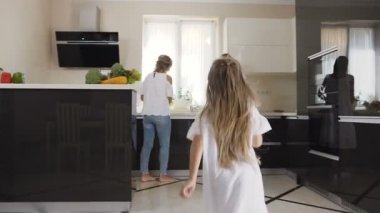 Küçük kız annesi ve ablası evde, tüm aile için kahvaltı yemek mutfakta tekrar karşılamak mutlu. Kız annesi ve kız kardeşi karşılamak için çalışır ve sarılmak ve öpmek için onları atar
