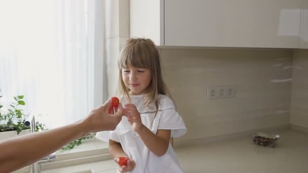 一个女人在吃饭前洗蔬菜, 她可爱的女儿坐在她旁边吃西红柿。健康食品概念。素食。女人和孩子。烹饪 — 图库视频影像