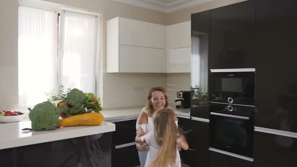 Mãe com filha divertida girando em torno de si mesma em casa na cozinha. Mulher bonita em uma roupa leve levanta sua menina encantadora e começa a girar alegremente em torno de si mesma e sorri. Feliz. — Vídeo de Stock