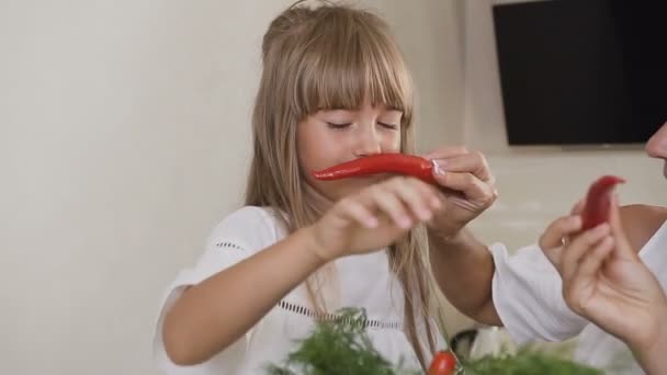 Atraktivní fun rodina se baví s chilli papričky doma v kuchyni. Dívky s dlouhými vlasy v bílých šatech učinit knír s chili paprika a zobrazit je k sobě navzájem. Zábava rodina v — Stock video