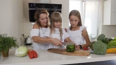 Anne ve kızları yemek mutfakta iki: kadın keser sebze, bir salata yapmak için yeşil biber ve kızlar öğretir. Anne ve iki kız şirin aile vejetaryen salata evde hazırlamak
