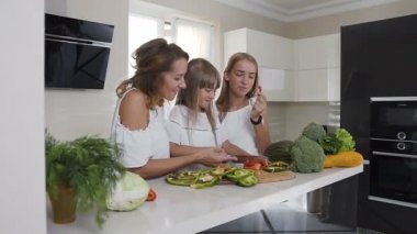 Mutlu anne ve iki kızları pişirme sebze yemek için ev mutfak. Gıda, sağlıklı beslenme, Aile